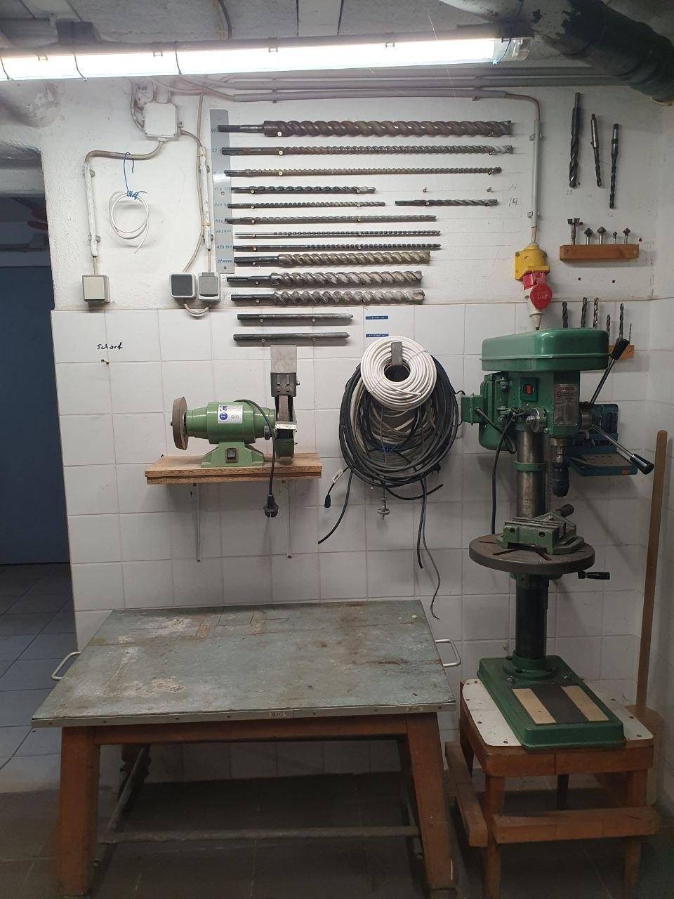 Professionelle Werkstatt mit Bohrmaschine, Schleifbock und einer Auswahl an Bohrern an der Wand.