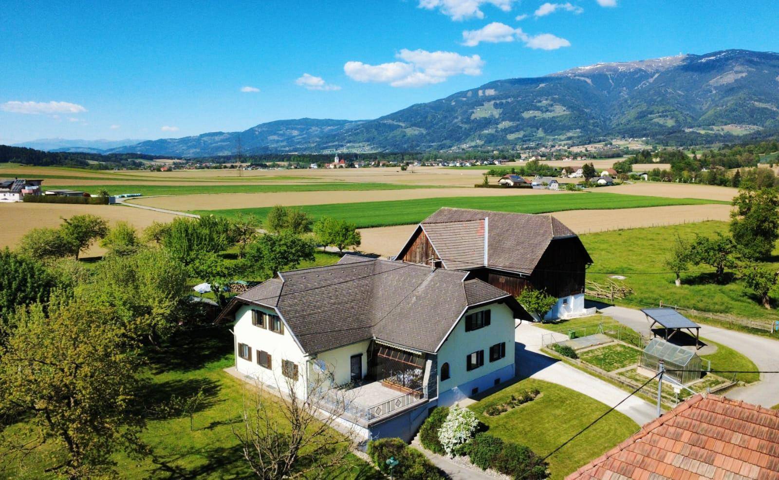 Weitläufiges Anwesen mit Wohnhaus und Scheune, umgeben von Feldern und Bergen unter blauem Himmel.