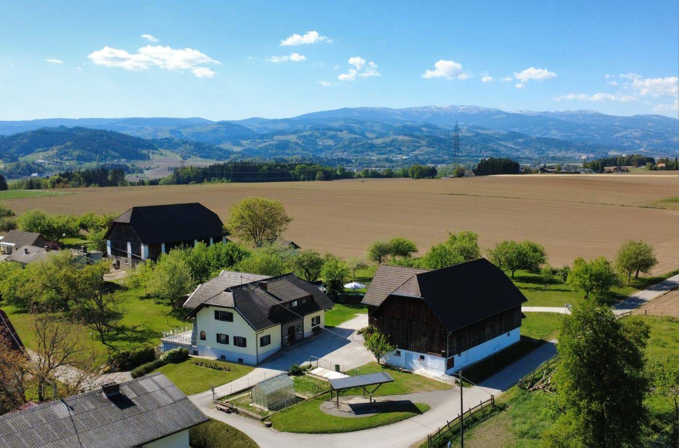 Panoramablick auf das Anwesen mit Wohnhaus und Scheune, eingebettet in weite Felder und hügelige Landschaft.