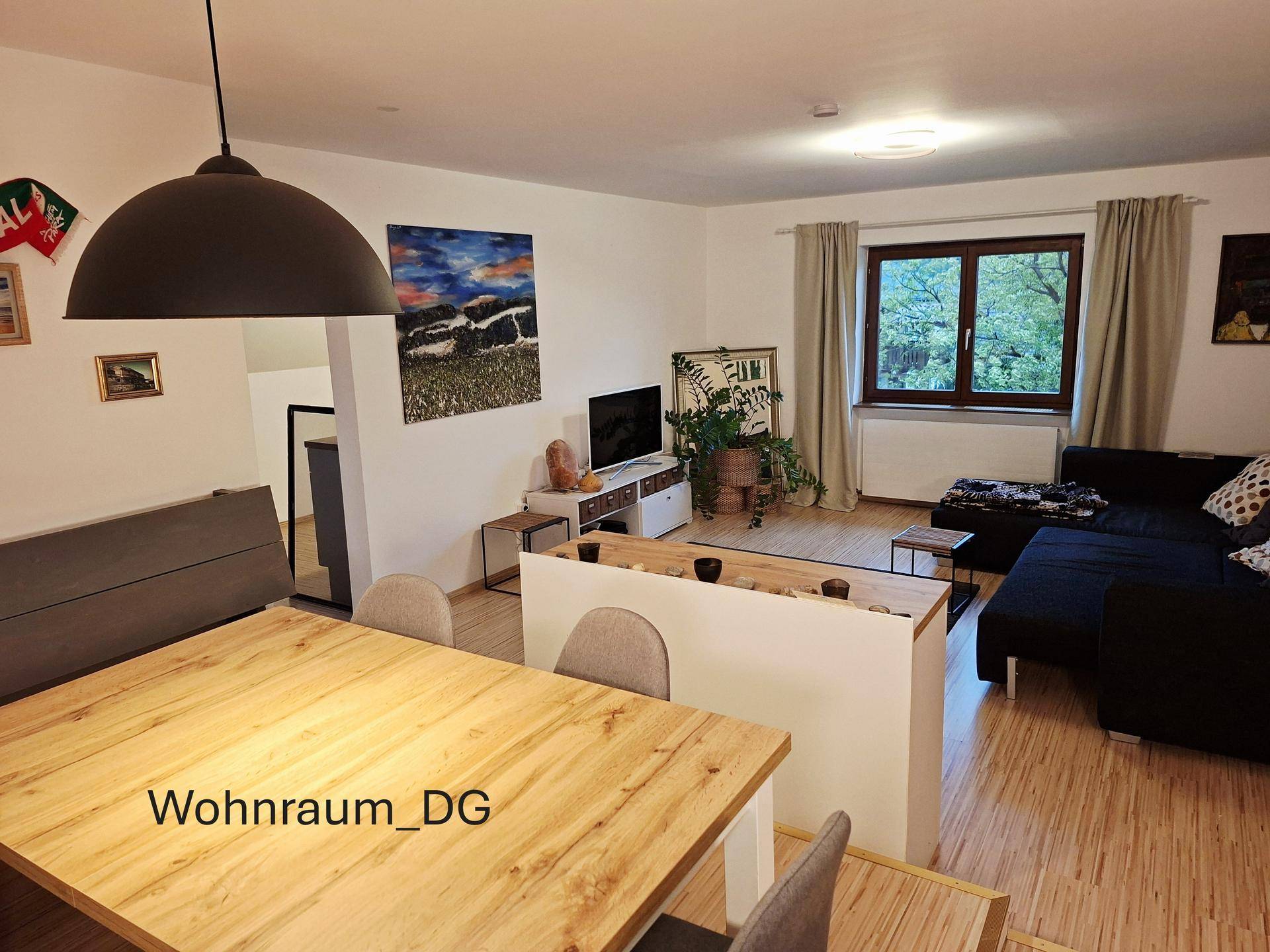Offener Wohn- und Essbereich im Dachgeschoss mit Holztisch, Sofa und Blick ins Grüne.