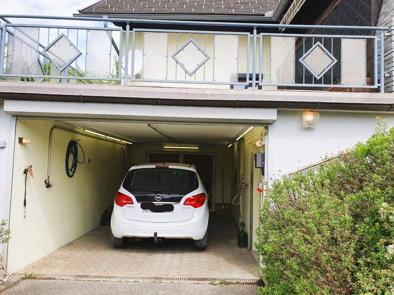 Integrierte Garage mit einem geparkten Auto und einem kleinen Balkon darüber mit Metallgeländer.