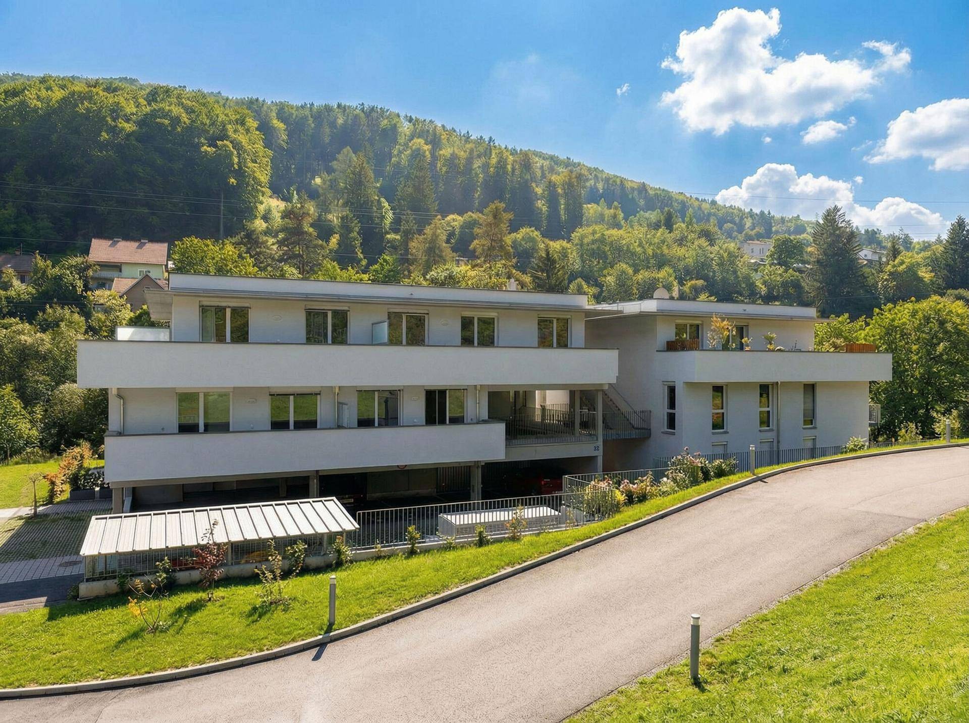 Ansicht der modernen Wohngebäude mit Balkonen und Terrassen, eingebettet in eine grüne Hügellandschaft.