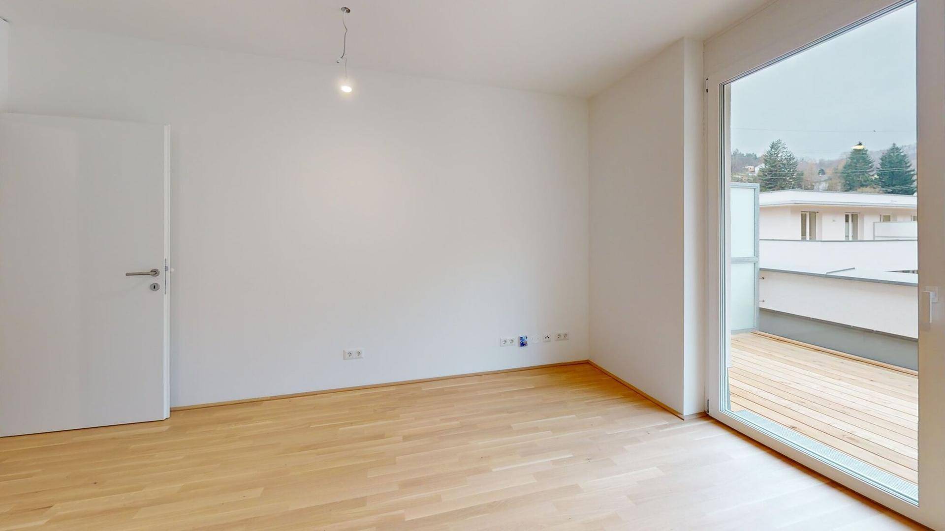 Leeres Schlafzimmer mit hellem Holzboden und großem Fenster mit Zugang zur Holzterrasse.