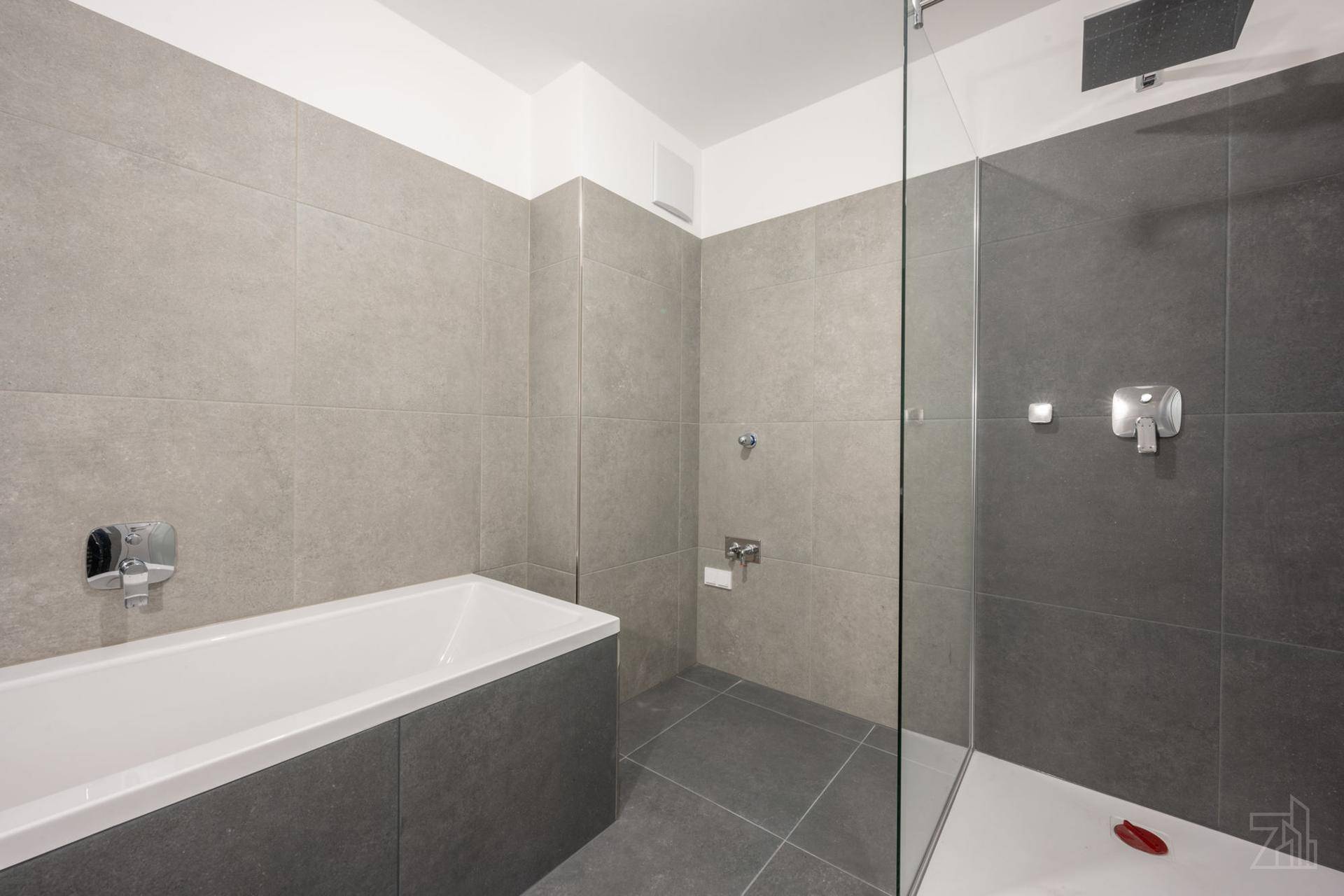 Zeitgemäßes Badezimmer mit Badewanne, begehbarer Dusche und grauen Wand- und Bodenfliesen.