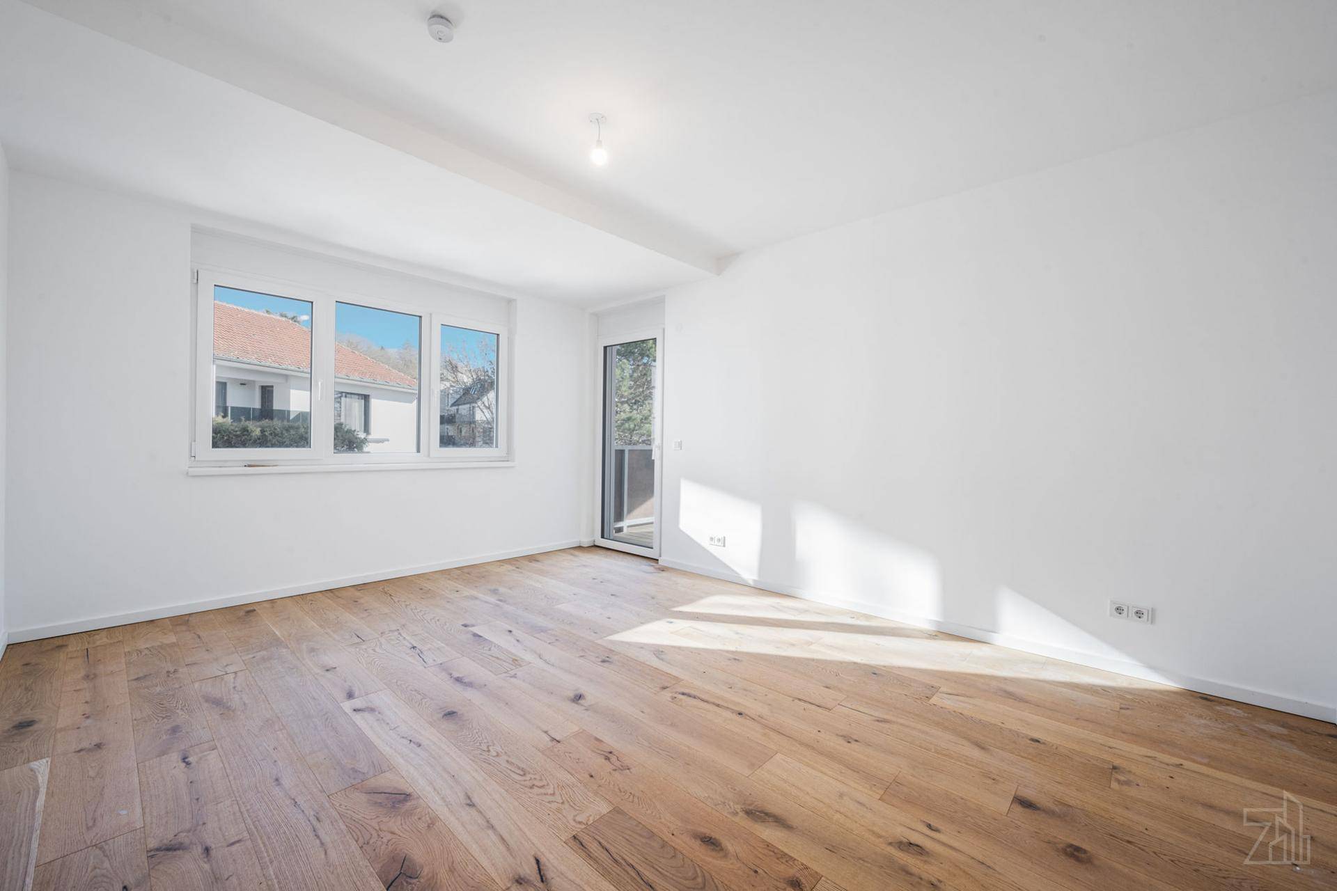 Leeres Zimmer mit Holzboden und viel Tageslicht, ideal als Schlaf- oder Arbeitszimmer.