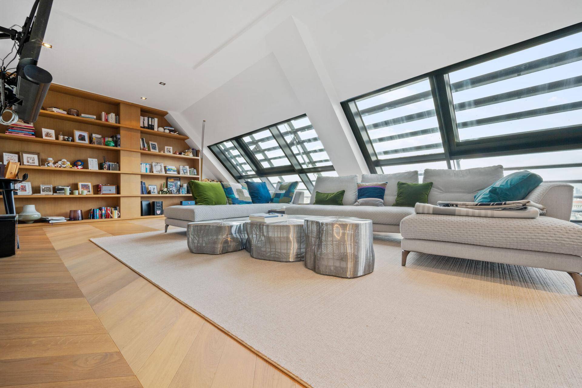 Helles Wohnzimmer mit großer Eckcouch, Bücherregal und schrägen Fenstern mit Ausblick.