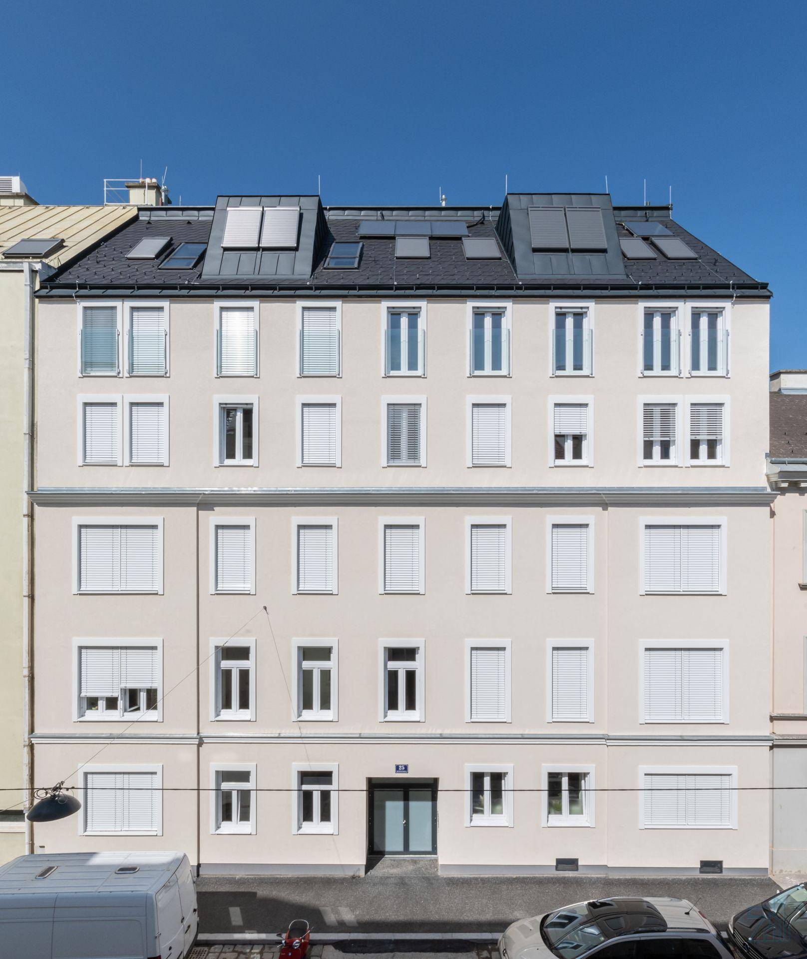 Moderne Fassade eines Mehrfamilienhauses mit vielen Fenstern und Rollläden unter blauem Himmel.