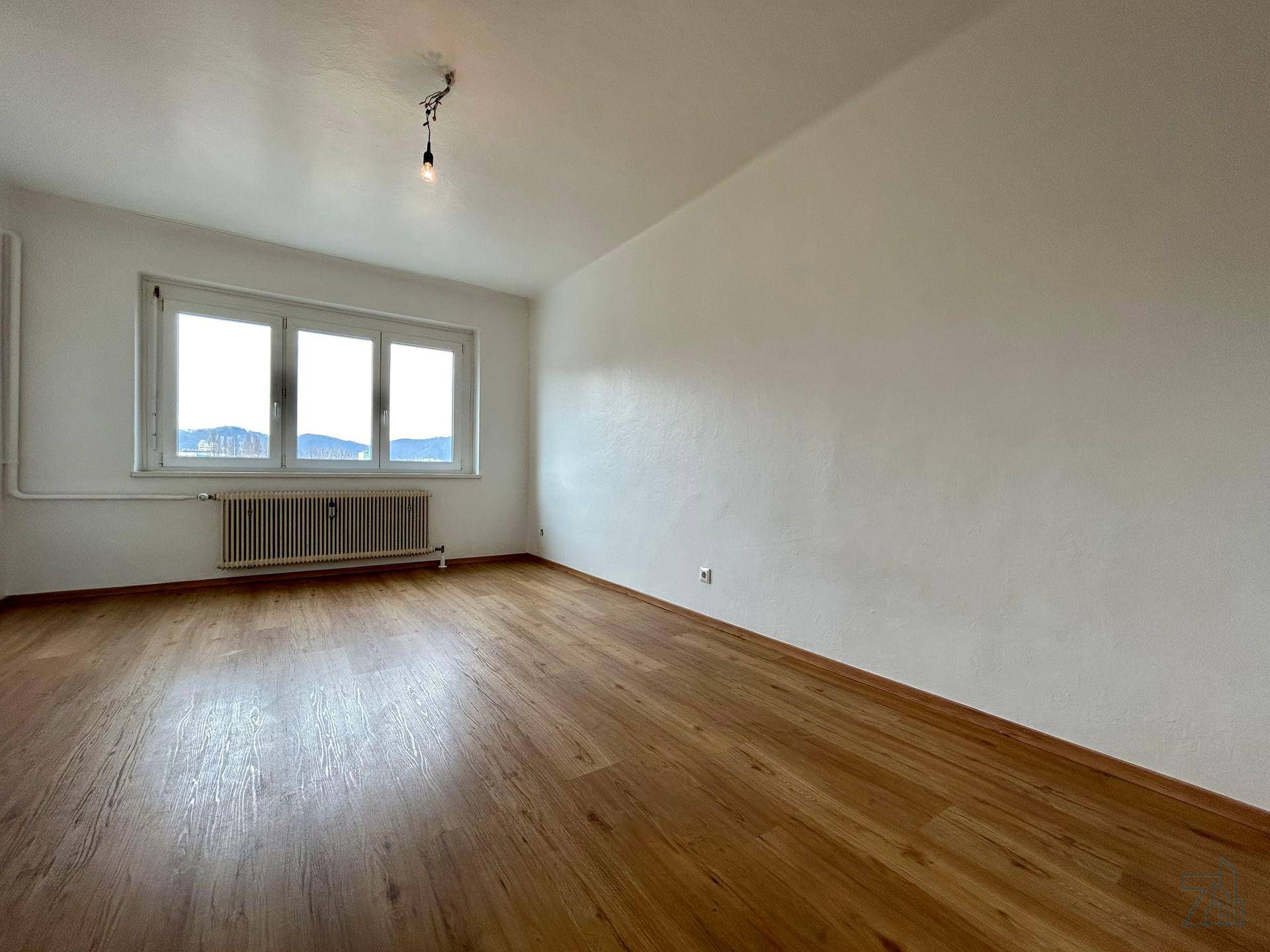 Geräumiges Schlafzimmer mit Holzboden und großem Fenster, das viel Tageslicht spendet.