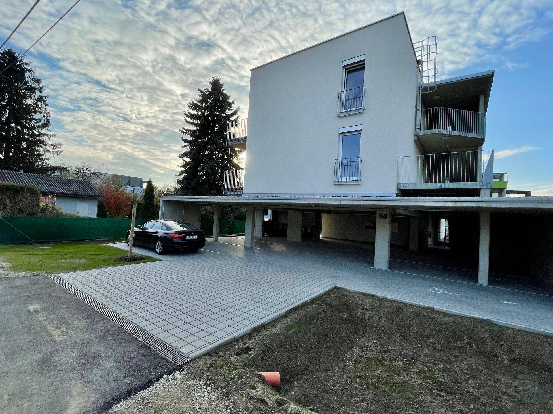 Außenansicht des modernen Gebäudes mit überdachten Parkplätzen und einem Auto.