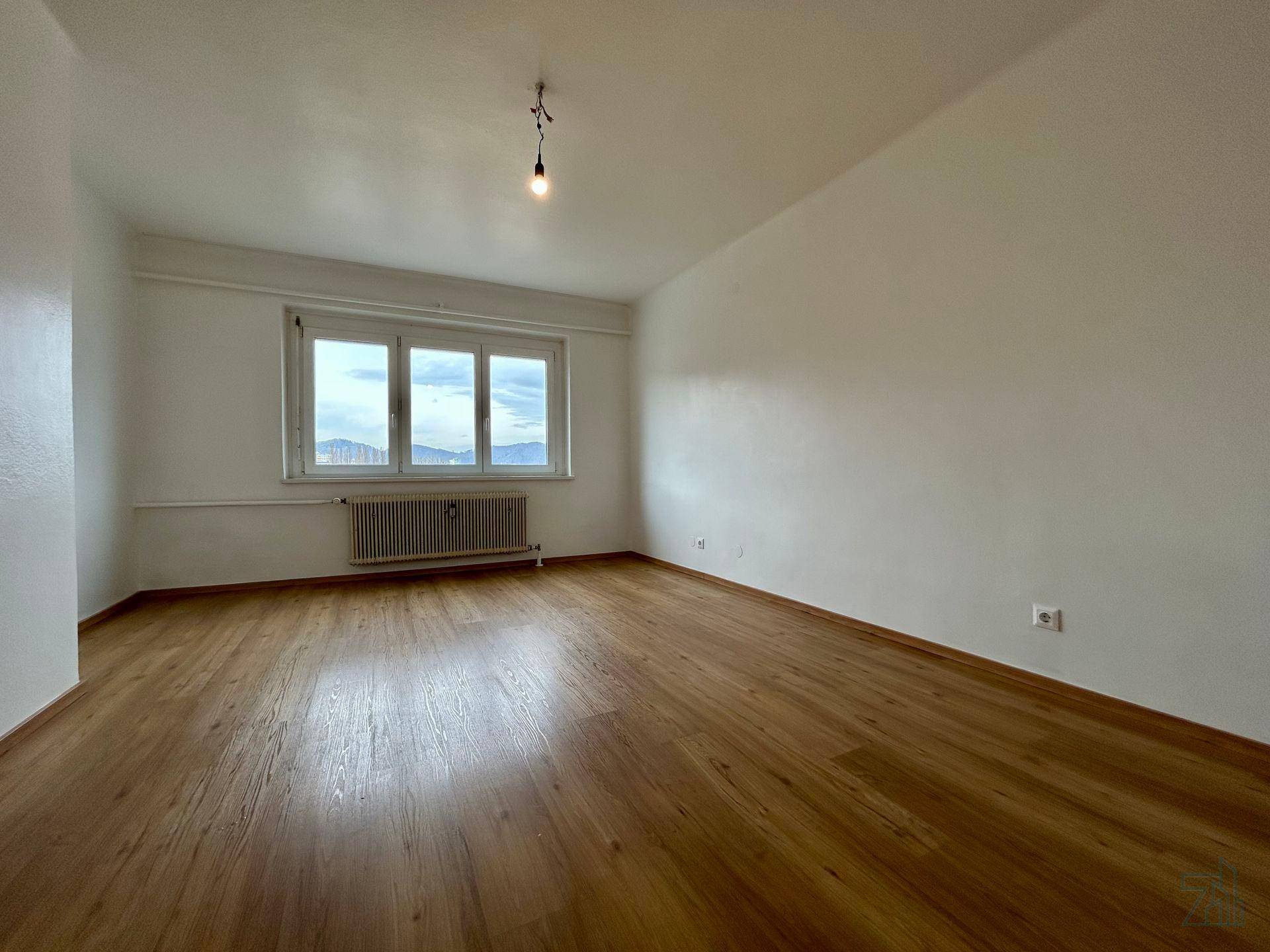Helles Schlafzimmer mit Holzboden und großem Fenster, das einen weiten Blick bietet.