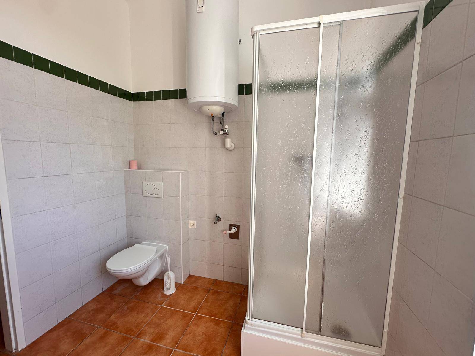 Badezimmer mit Duschkabine, wandhängendem WC und Boiler, ausgestattet mit weißen Fliesen.