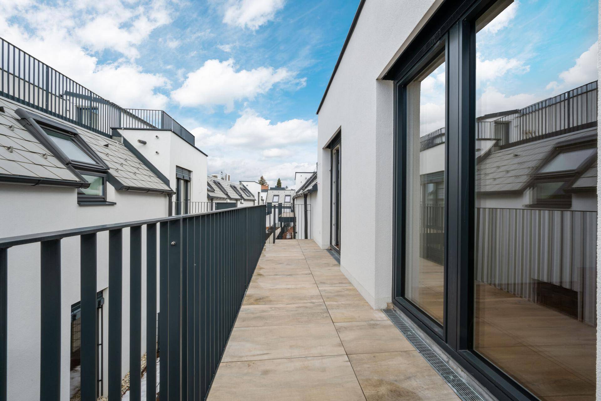 Langer Balkon mit Fliesenboden und Metallgeländer entlang der Hausfassade.