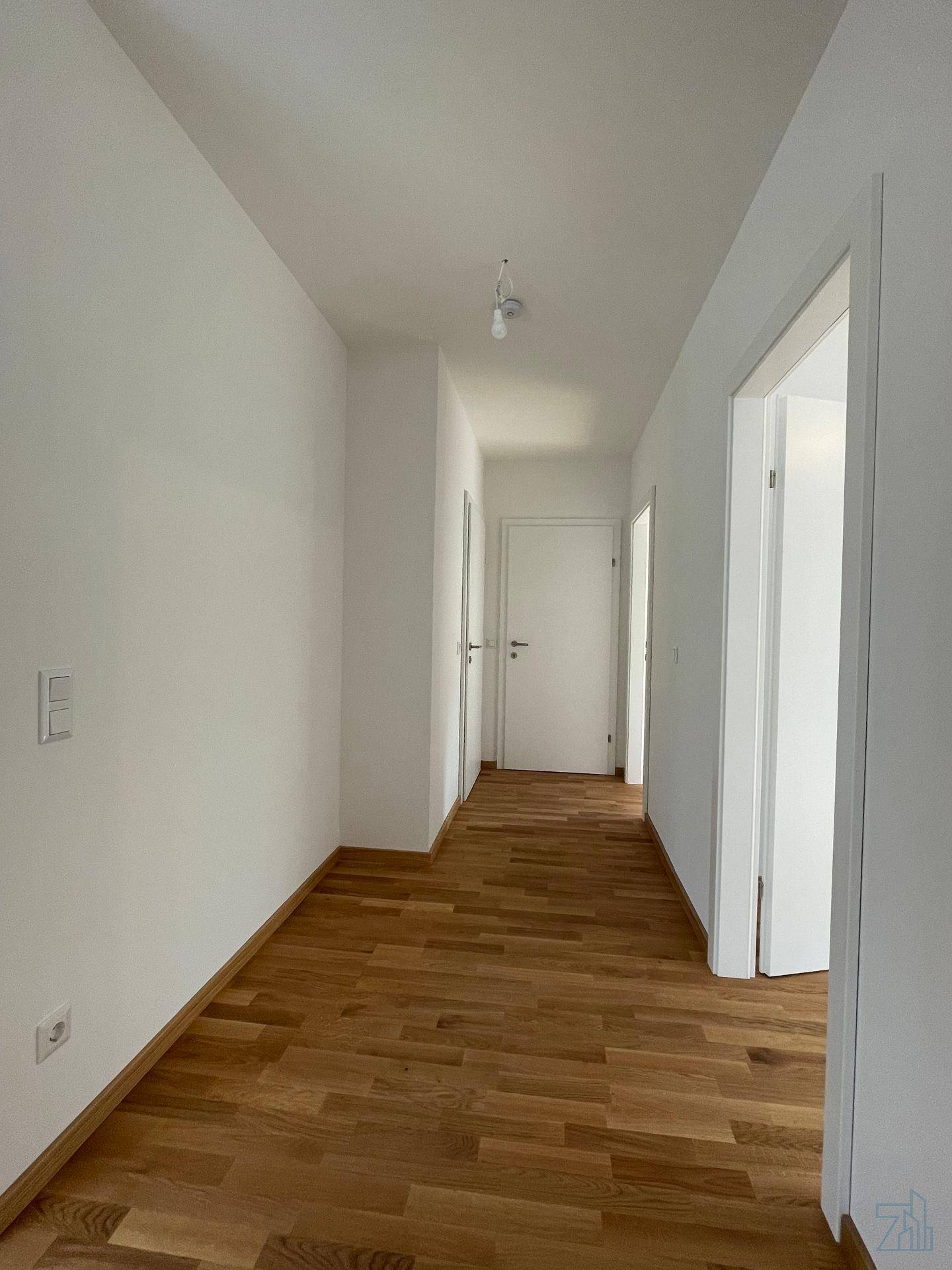 Langer, heller Flur mit Holzboden und mehreren Türen zu angrenzenden Räumen.