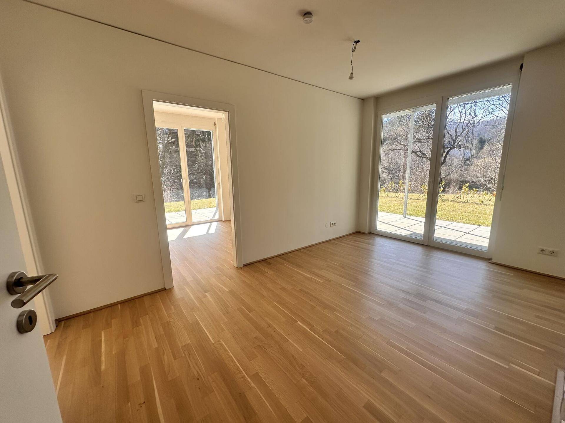Lichtdurchfluteter Raum mit Parkettboden und Zugang zu einer Außenterrasse.