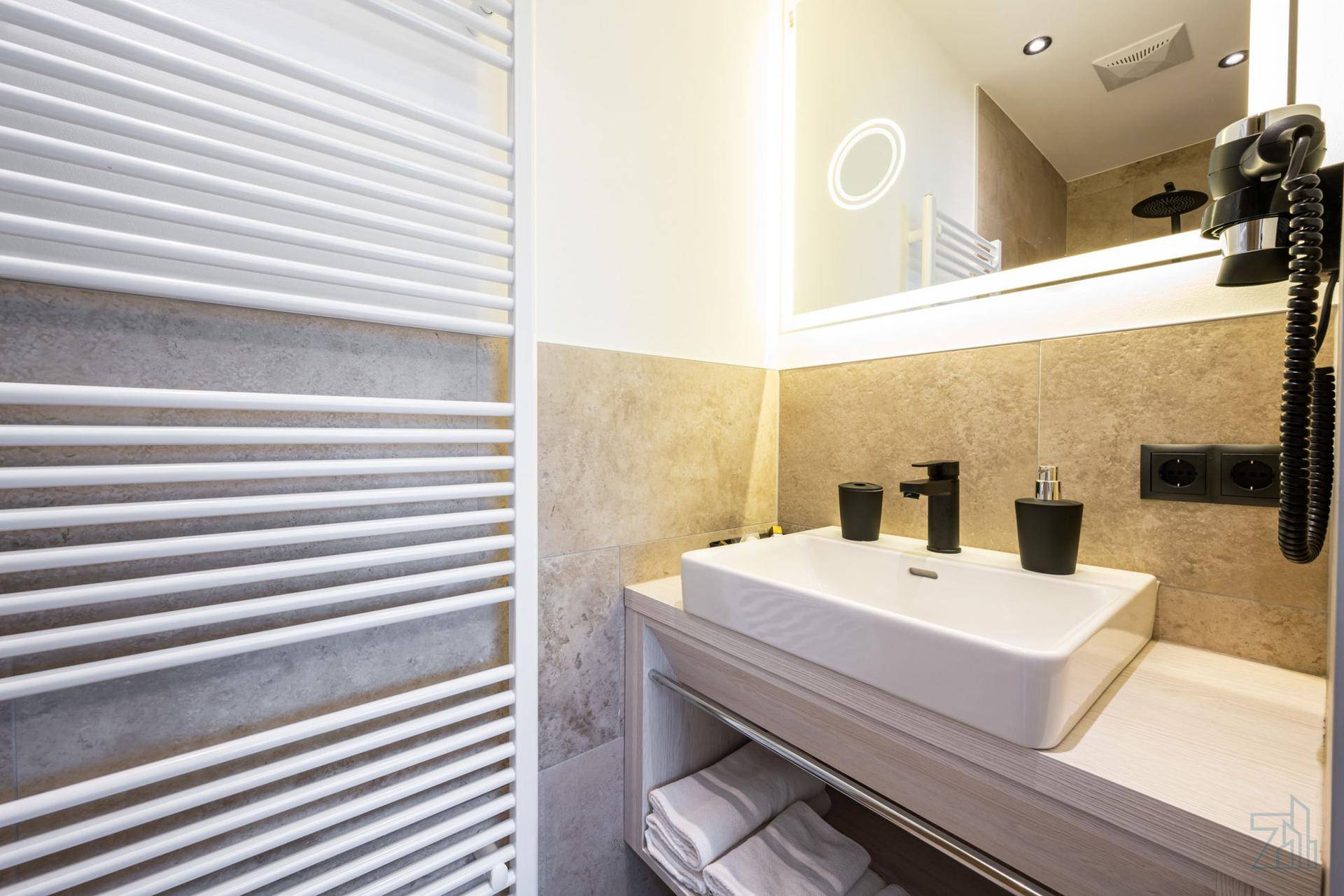 Modernes Badezimmer mit Einzelwaschbecken, beleuchtetem Spiegel und beheiztem Handtuchhalter.