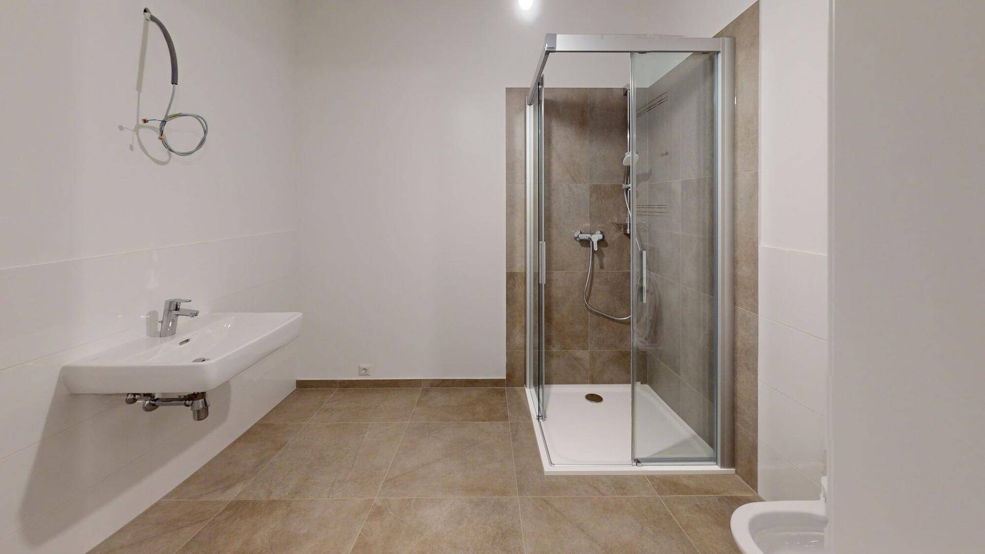 Modernes Badezimmer mit Duschkabine, Waschbecken und hellbraunen Fliesen in neuwertigem Zustand.