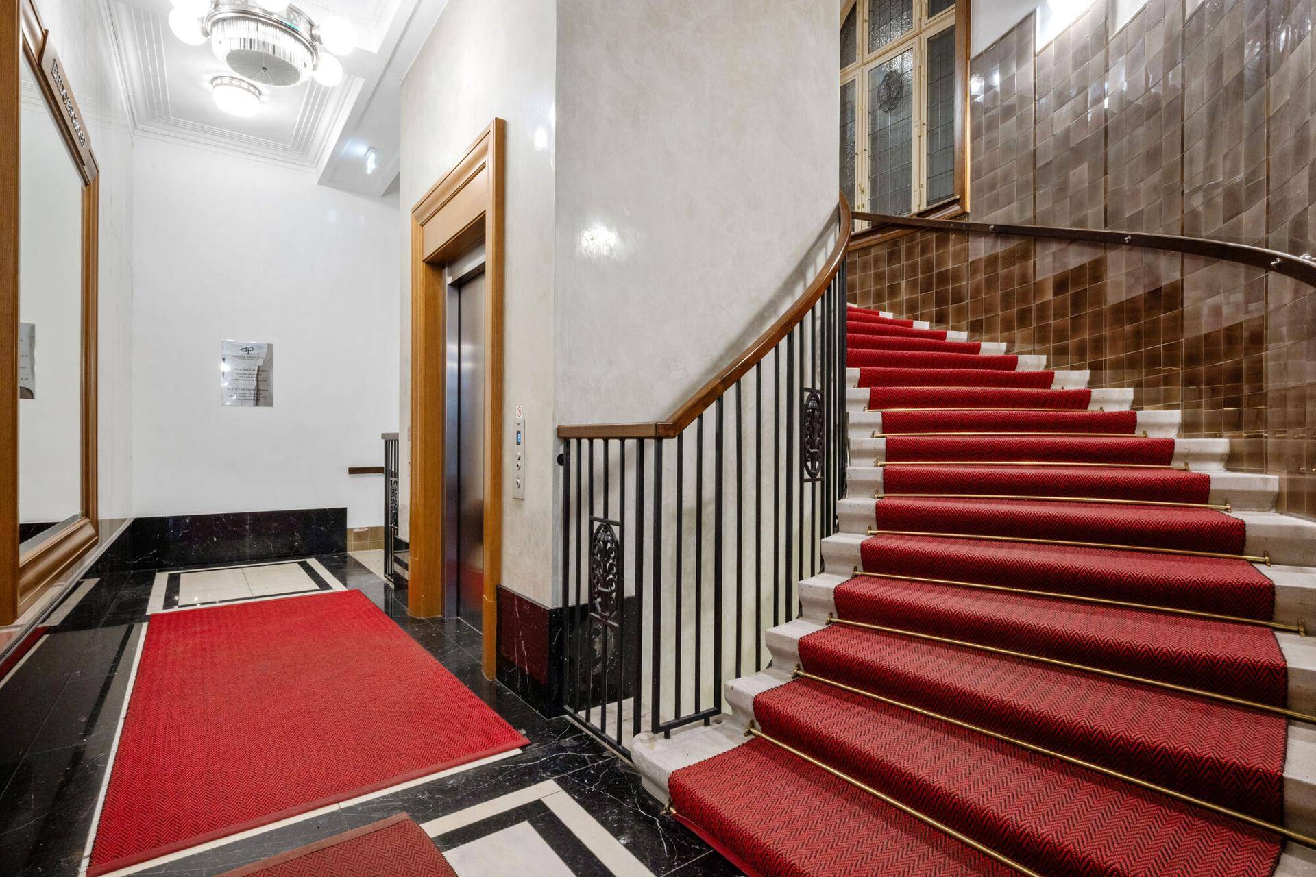 Elegantes Treppenhaus mit rotem Teppich und klassischem Aufzug in einem Altbau.