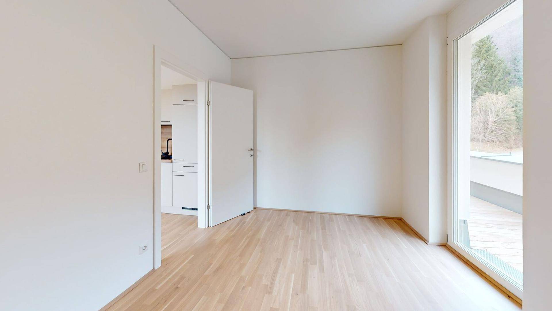 Heller Wohnbereich mit Parkettboden, Zugang zum Balkon und Blick in die angrenzende Küche.