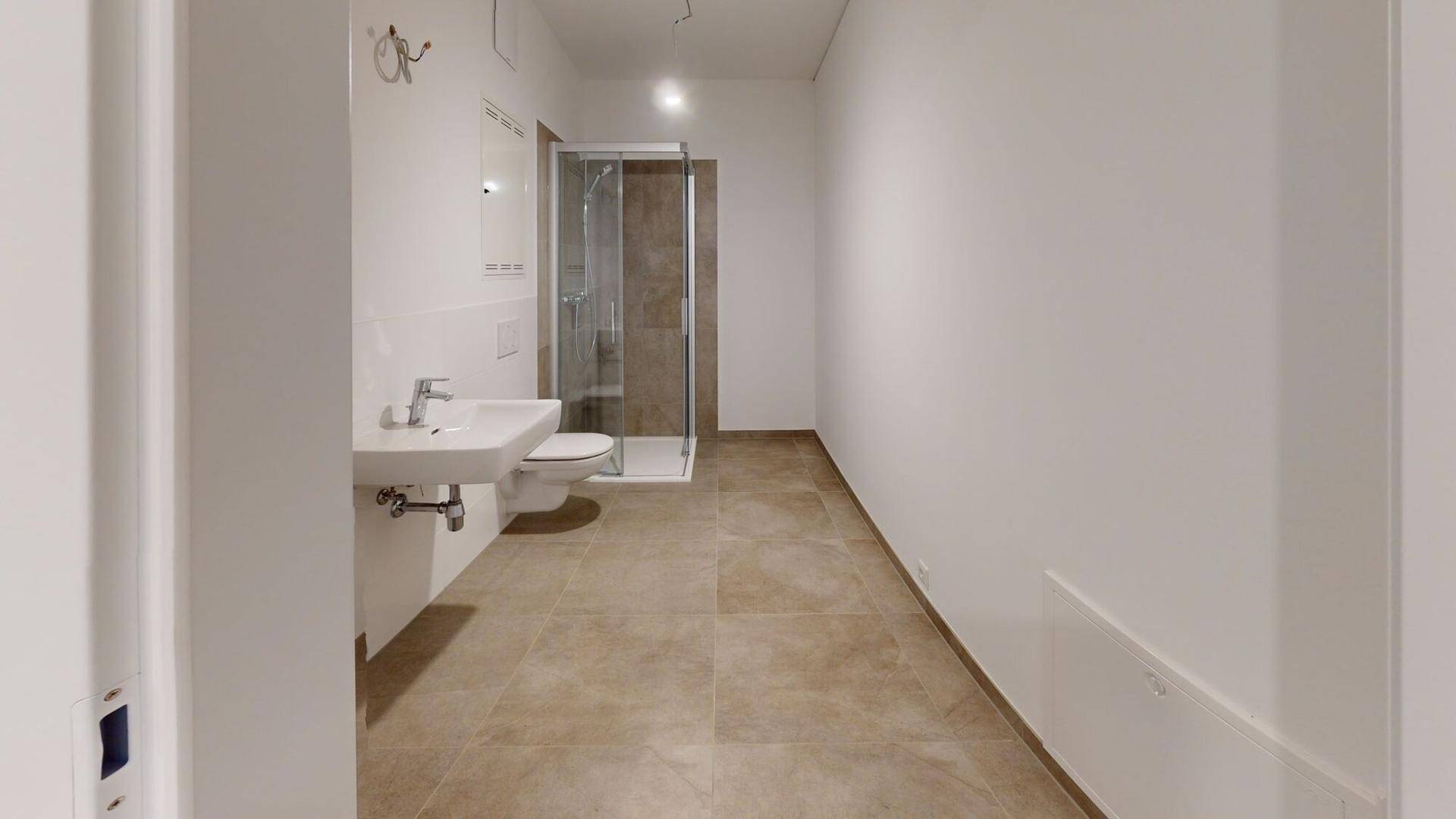 Modernes Badezimmer mit beigen Fliesen, wandhängendem WC und begehbarer Dusche.