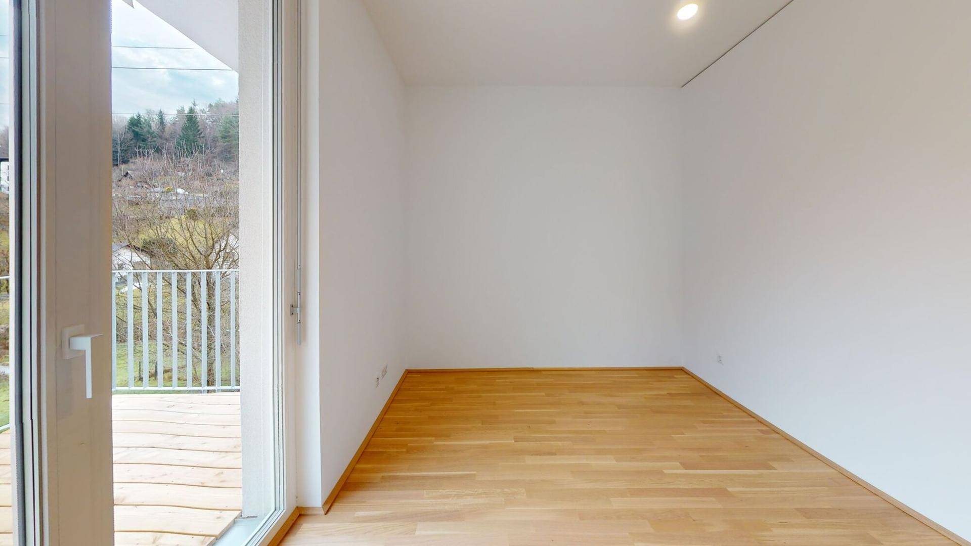 Geräumiges Zimmer mit Holzboden und großen Fenstern, die Zugang zu einem Balkon bieten.