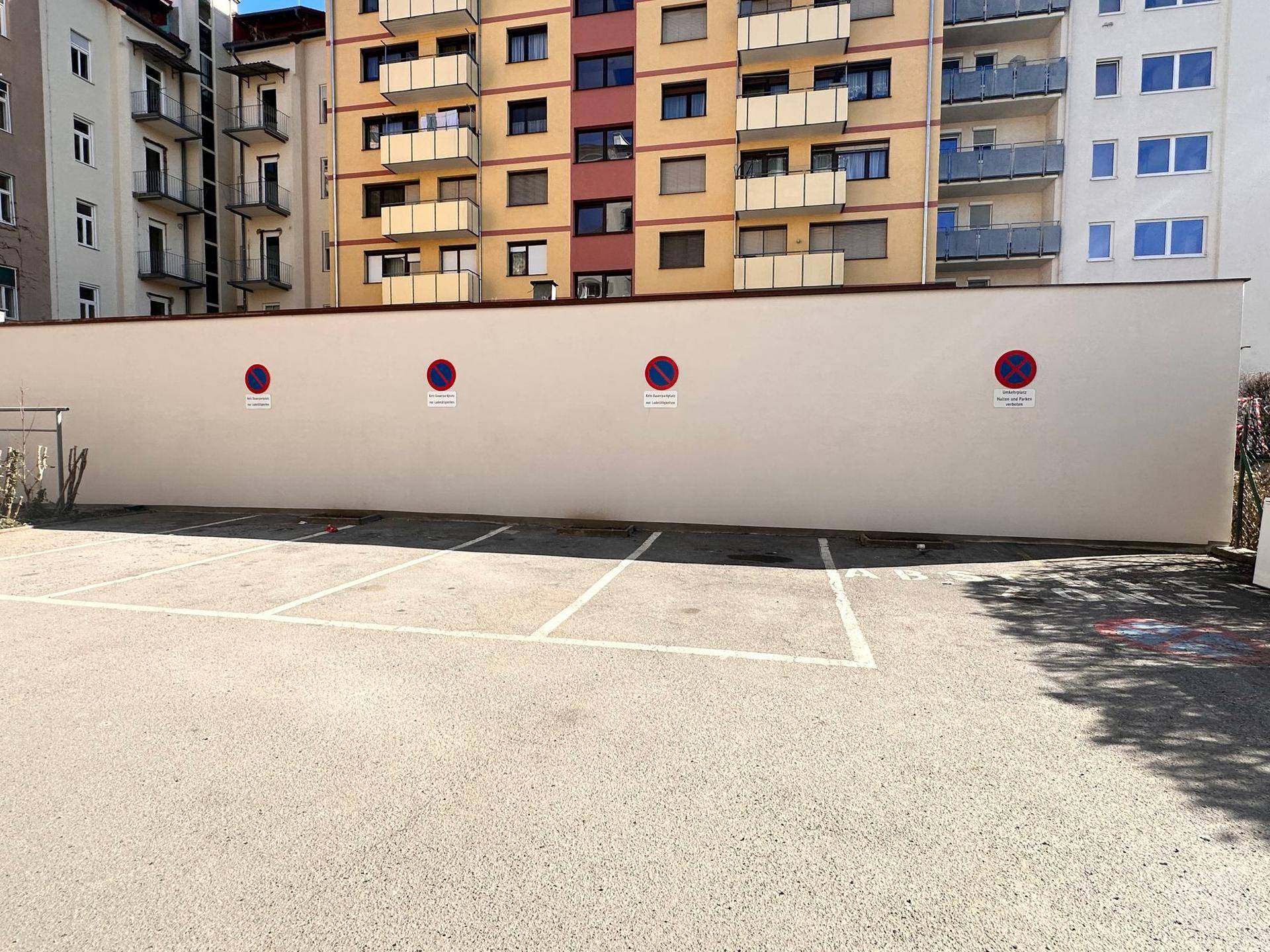 Außenparkplatz mit markierten Stellplätzen und einer hohen Wand im Hintergrund.