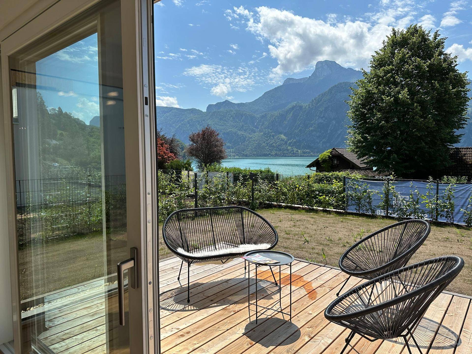 Sonniger Terrassenbereich mit modernen Outdoor-Möbeln und atemberaubendem Blick auf den See und die Berge.