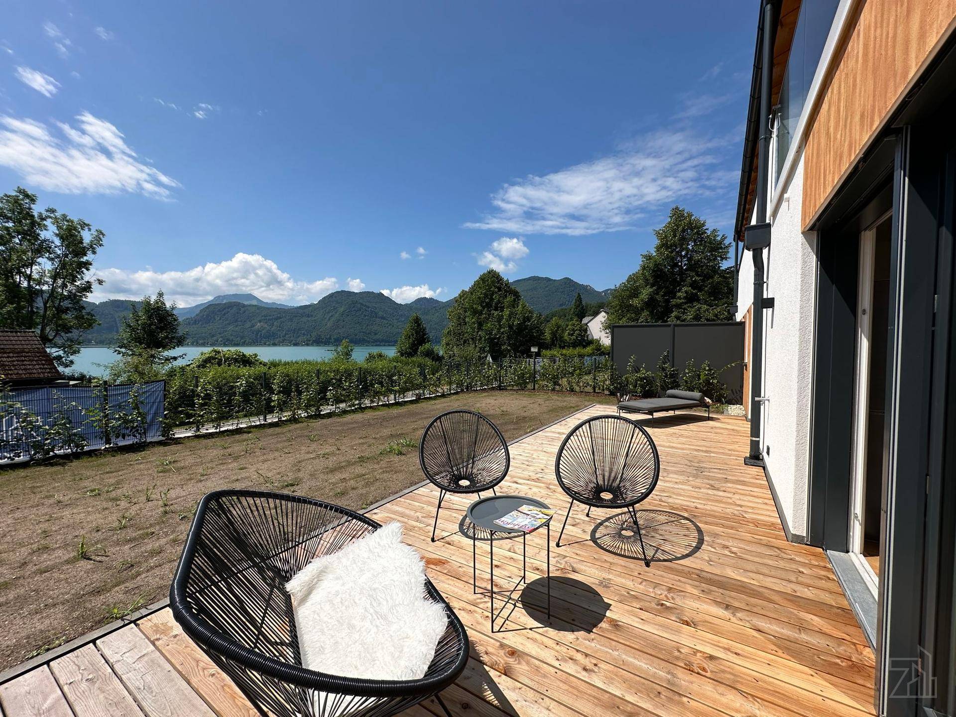 Geräumige Holzterrasse mit modernen Sitzgelegenheiten und weitem Blick auf den See und die Berge.