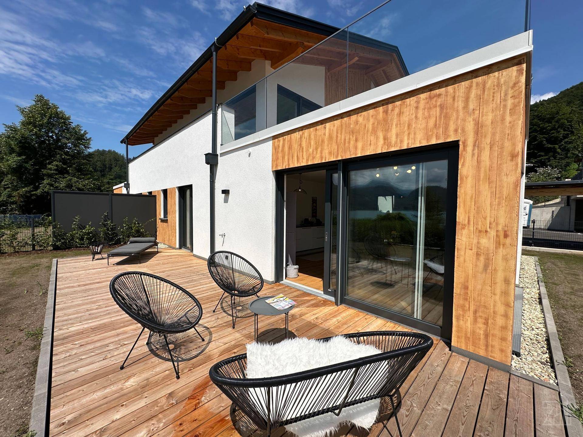 Moderne Architektur mit Holzfassade und großer Holzterrasse mit Seeblick.