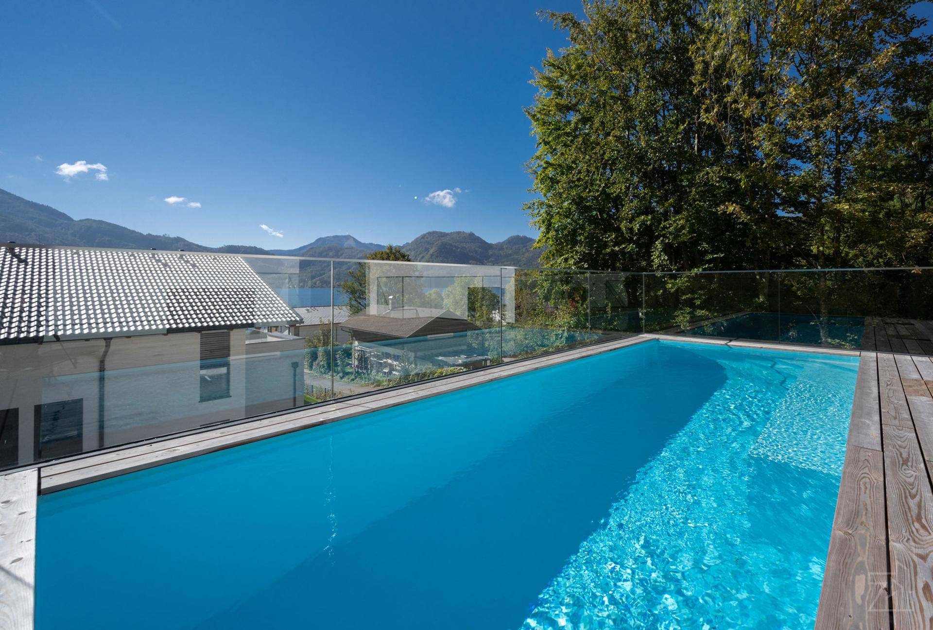 Moderner Außenpool mit Holzdeck und Panoramablick auf den See und die umliegenden Berge.