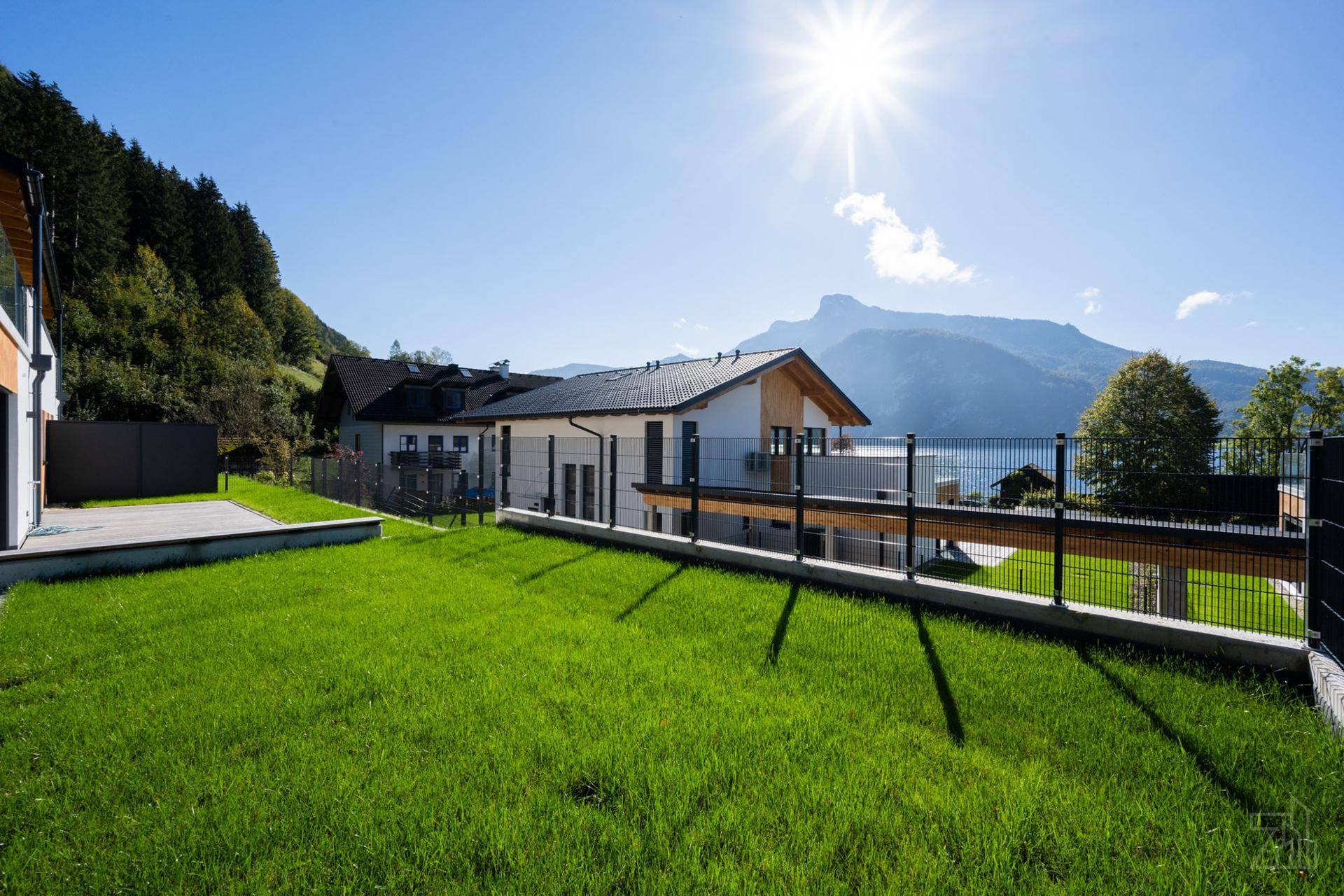 Gepflegter Rasen vor einem modernen Haus mit weitem Blick auf den See und die umliegenden Berge.