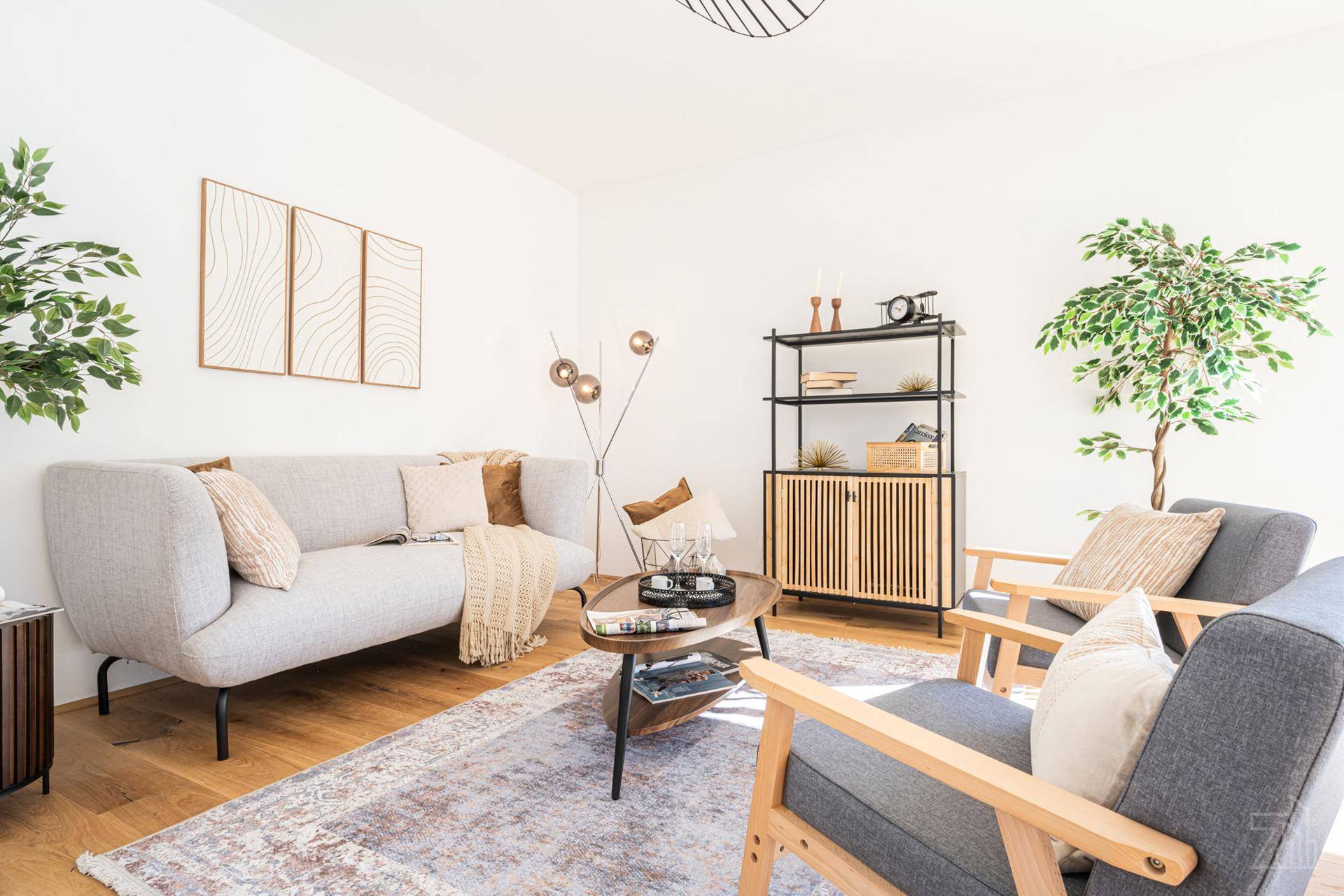 Helles Wohnzimmer mit modernem Sofa, bequemen Sesseln und Holzboden, dekoriert mit Pflanzen.