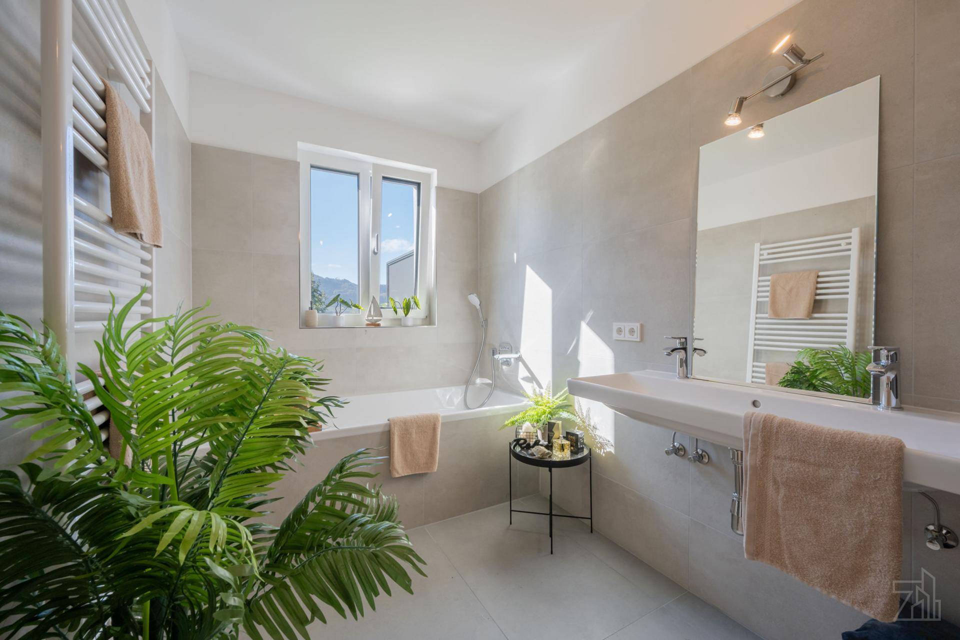 Modernes Badezimmer mit Badewanne, großem Spiegel und Fenster, hell gefliest und gut beleuchtet.
