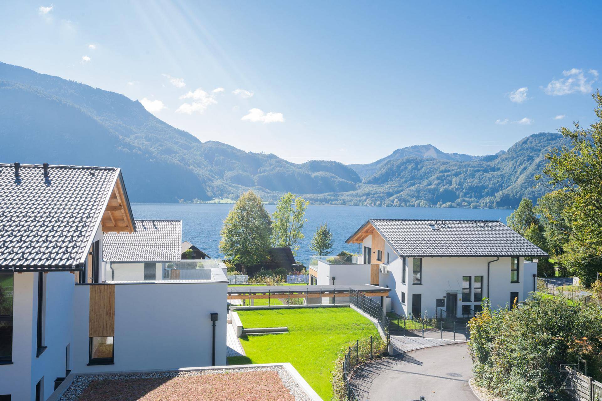 Siedlung moderner Häuser mit Blick auf den See und die umliegenden Berge an einem sonnigen Tag.