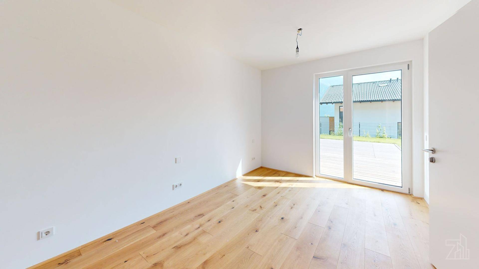 Leeres Schlafzimmer mit Holzboden und Zugang zu einem Außenbereich, hell und modern gestaltet.