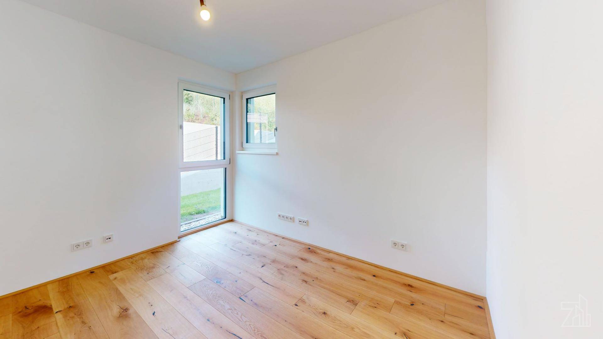 Helles, leeres Zimmer mit Holzboden und zwei Fenstern, ideal als Schlaf- oder Arbeitszimmer.