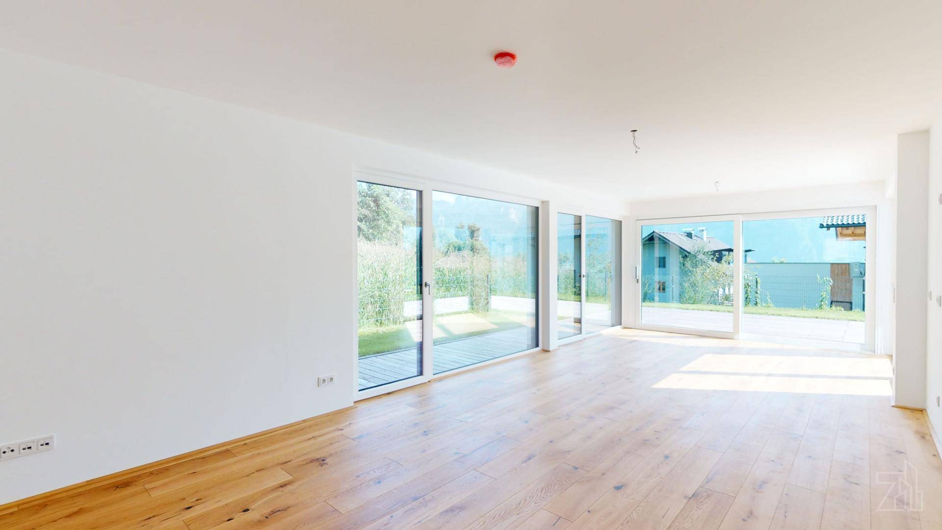 Geräumiger, heller Wohnbereich mit Holzboden und großen Fenstern zum Garten, noch unmöbliert.