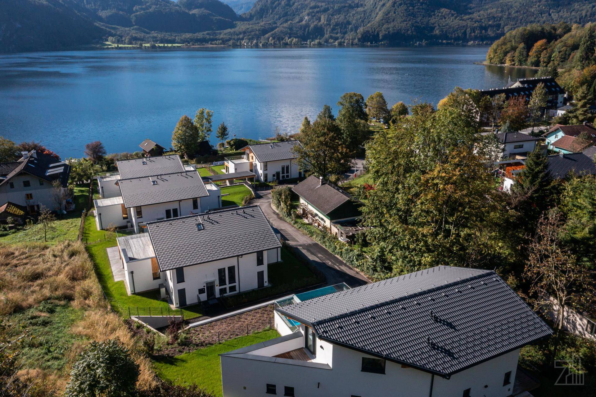 Luftaufnahme von modernen Häusern am Seeufer mit Bergblick und umliegender Natur.