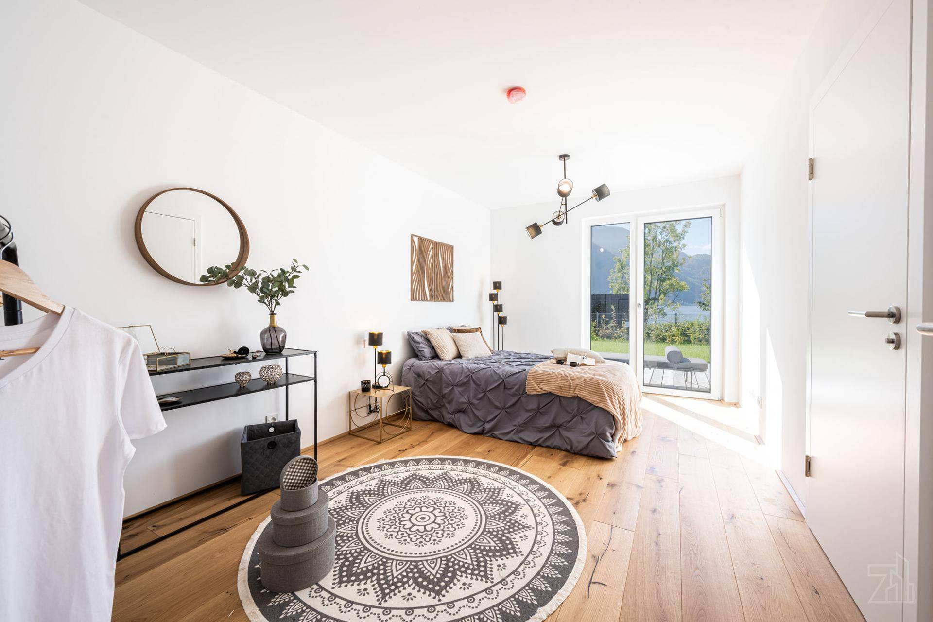 Helles Schlafzimmer mit Holzboden, modernem Bett und Zugang zu einer Terrasse mit Seeblick.