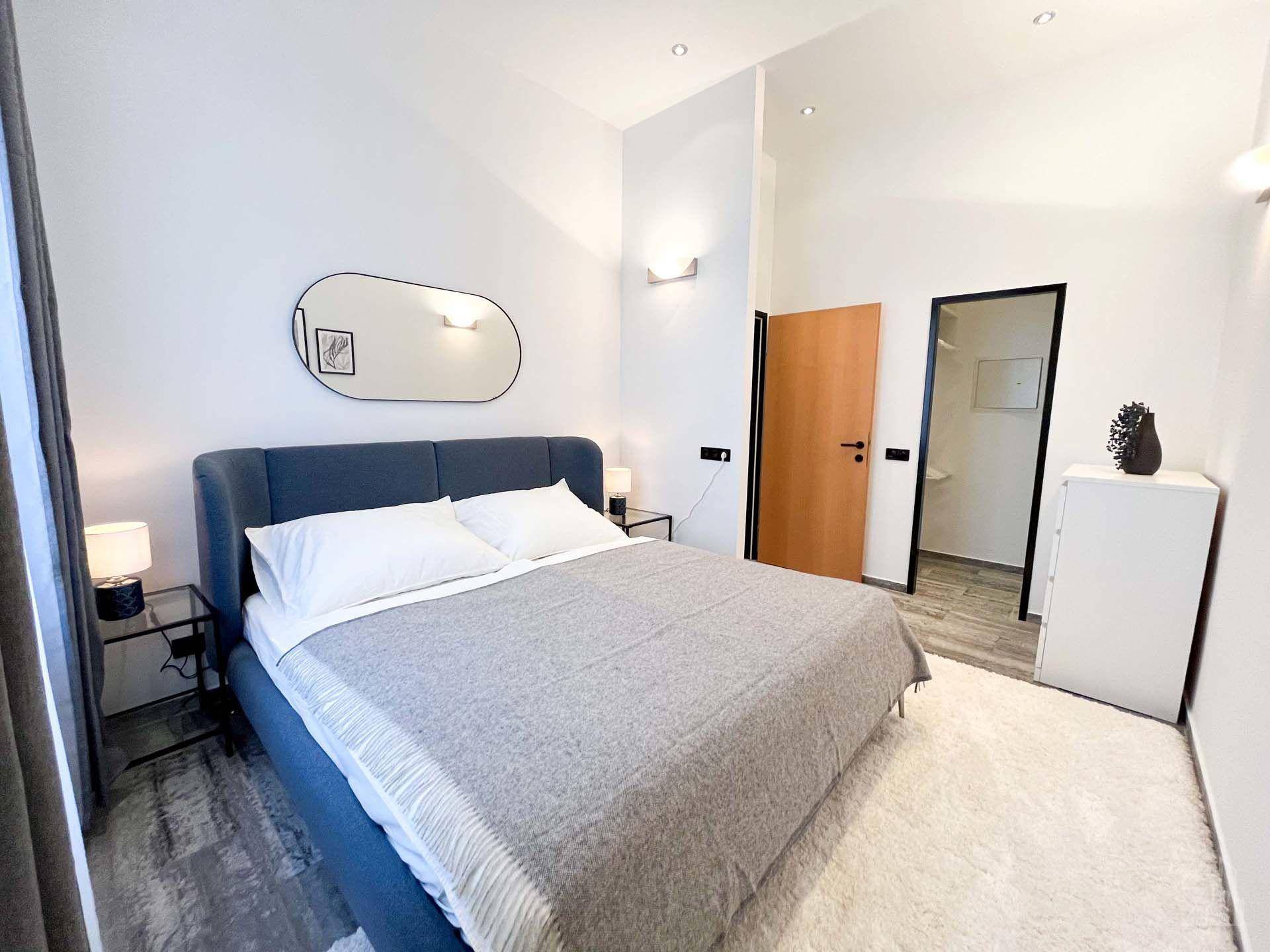 Modernes Schlafzimmer mit blauem Polsterbett, hellem Boden und direktem Zugang zum Badezimmer.
