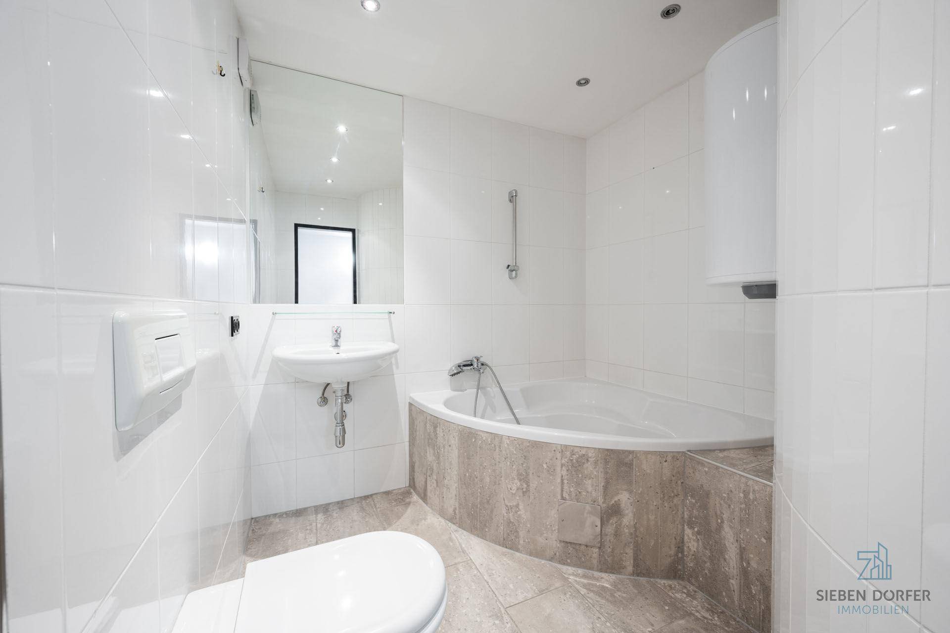 Modernes Badezimmer mit Eckbadewanne, weißen Fliesen und Wandspiegel.