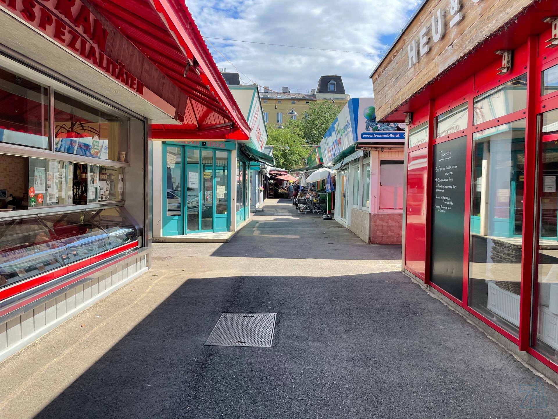 Gasse mit Marktständen und Geschäften unter roten und blauen Markisen.