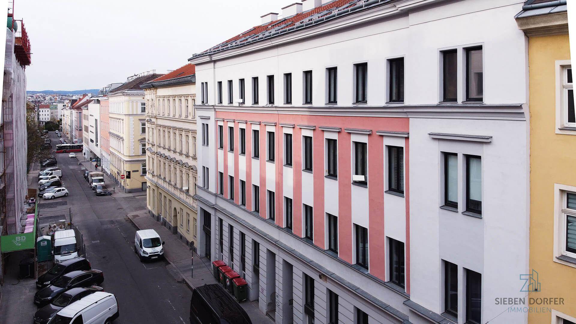 Blick von oben auf die Straße mit parkenden Autos und der Gebäudefassade.