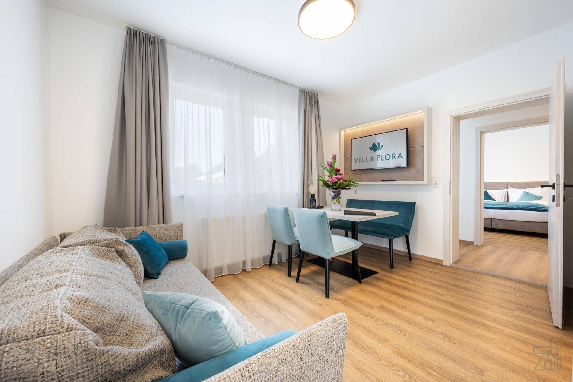 Heller Wohn-Essbereich mit Sofa, Esstisch und modernem TV, verbunden mit dem Schlafzimmer.