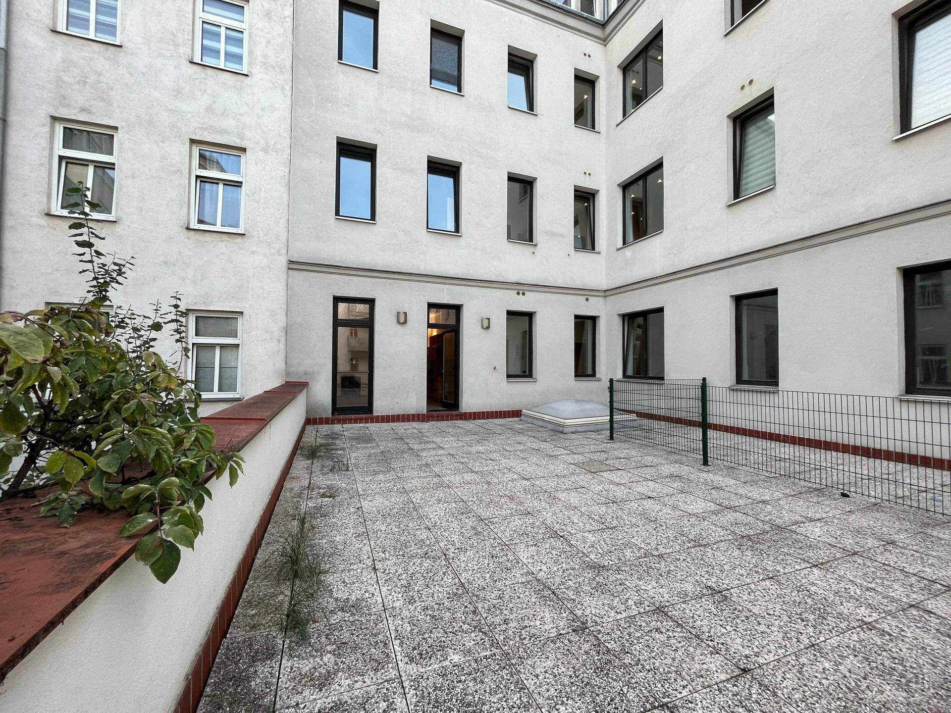 Innenhof mit gepflasterter Fläche, umgeben von Gebäudefassaden und einem kleinen Netz.