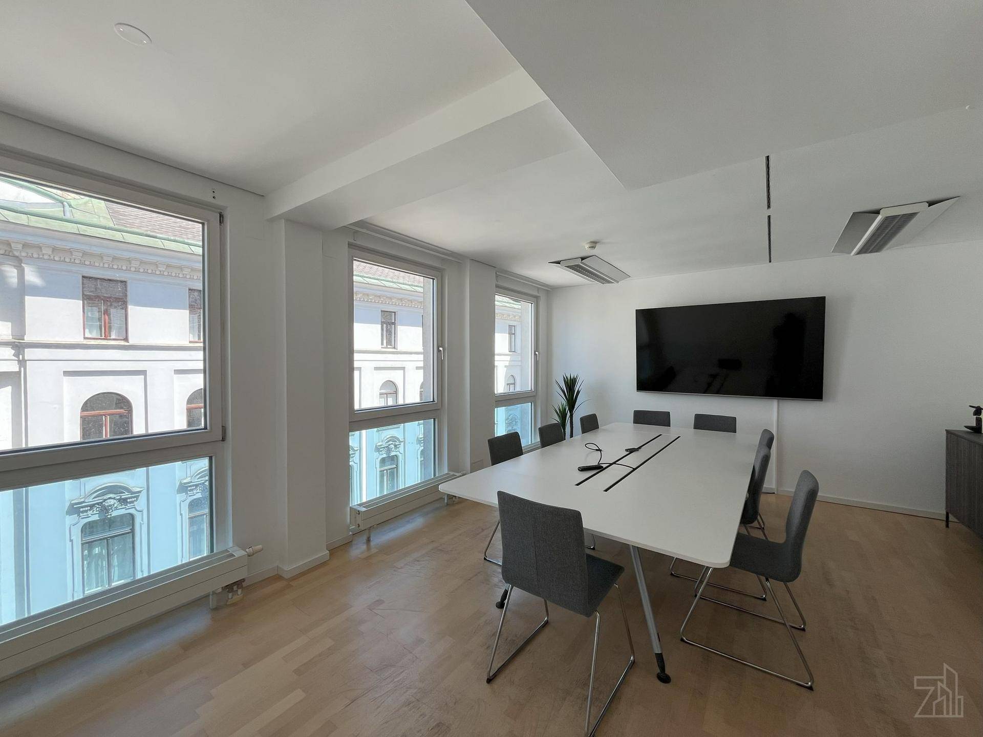 Moderner Konferenzraum mit großem Tisch, Stühlen, Wandbildschirm und hohen Fenstern mit Stadtblick.