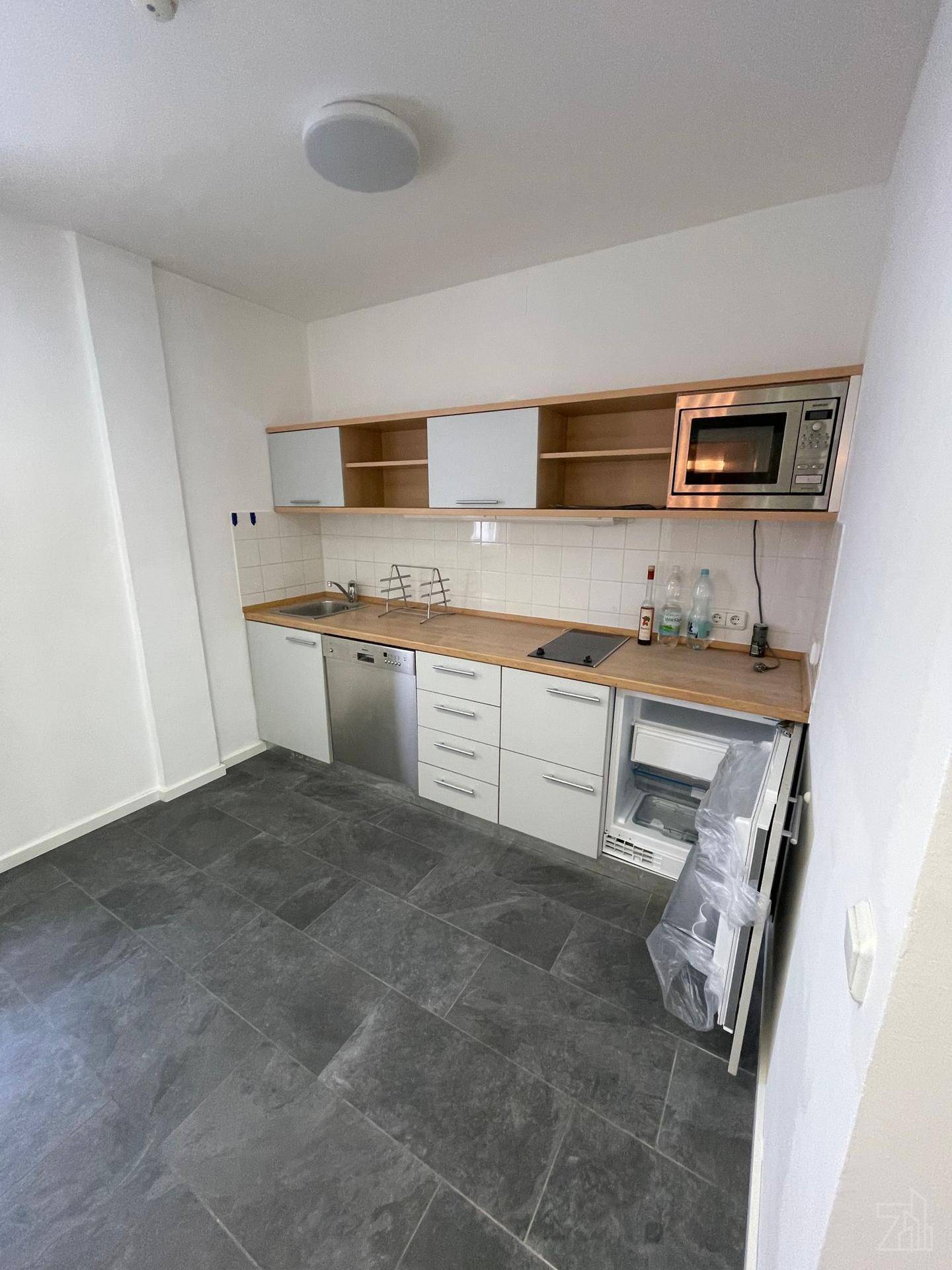 Kleine, funktionale Küchenzeile mit weißen Schränken, Holztheke und integrierten Geräten auf Fliesenboden.
