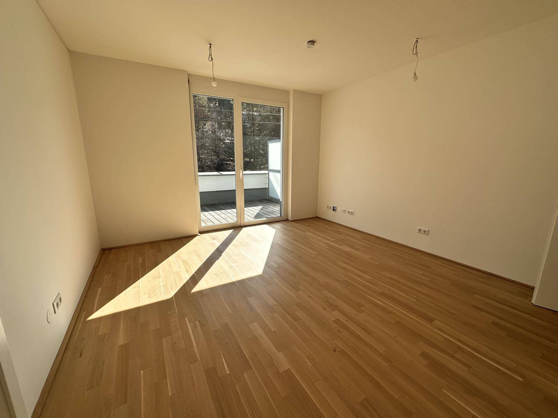 Modernes, leeres Zimmer mit Holzboden und großen Terrassentüren, bereit für die individuelle Einrichtung.