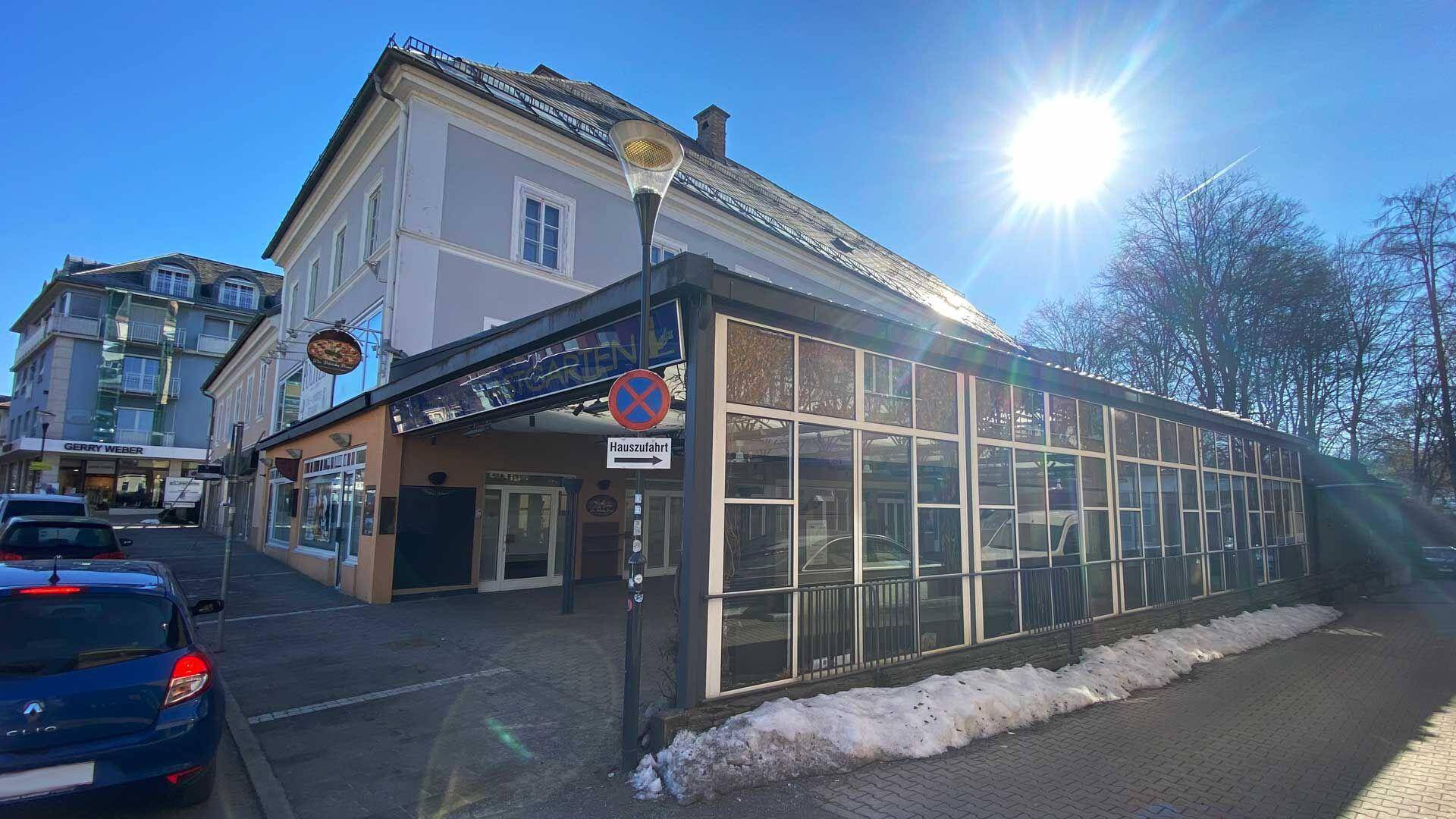Gebäudeansicht mit einer modernen Glasfassade und einem angrenzenden Altbau unter strahlendem Sonnenschein.