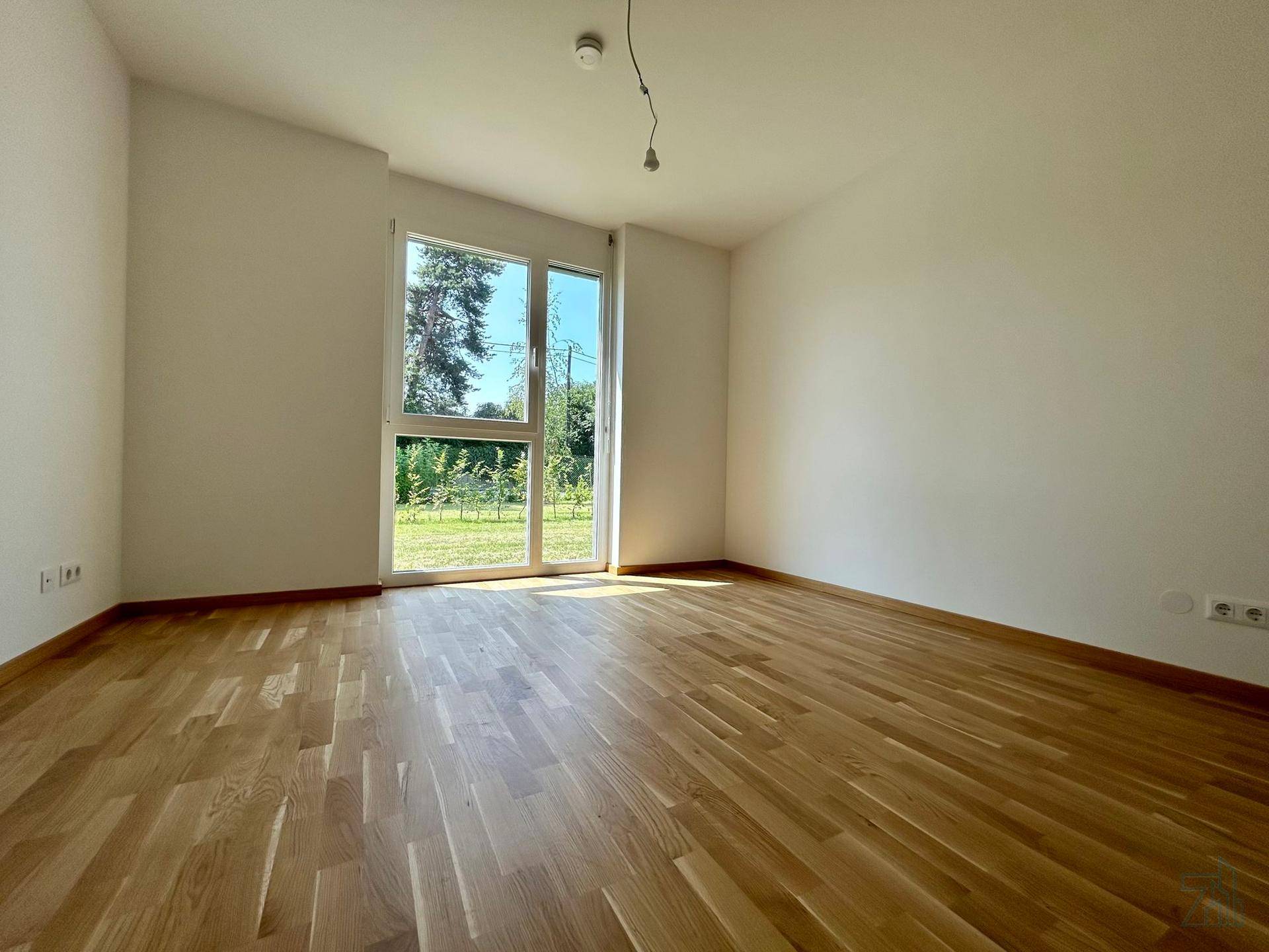 Helles Zimmer mit Parkettboden und großen Fenstern, die viel Tageslicht hereinlassen.