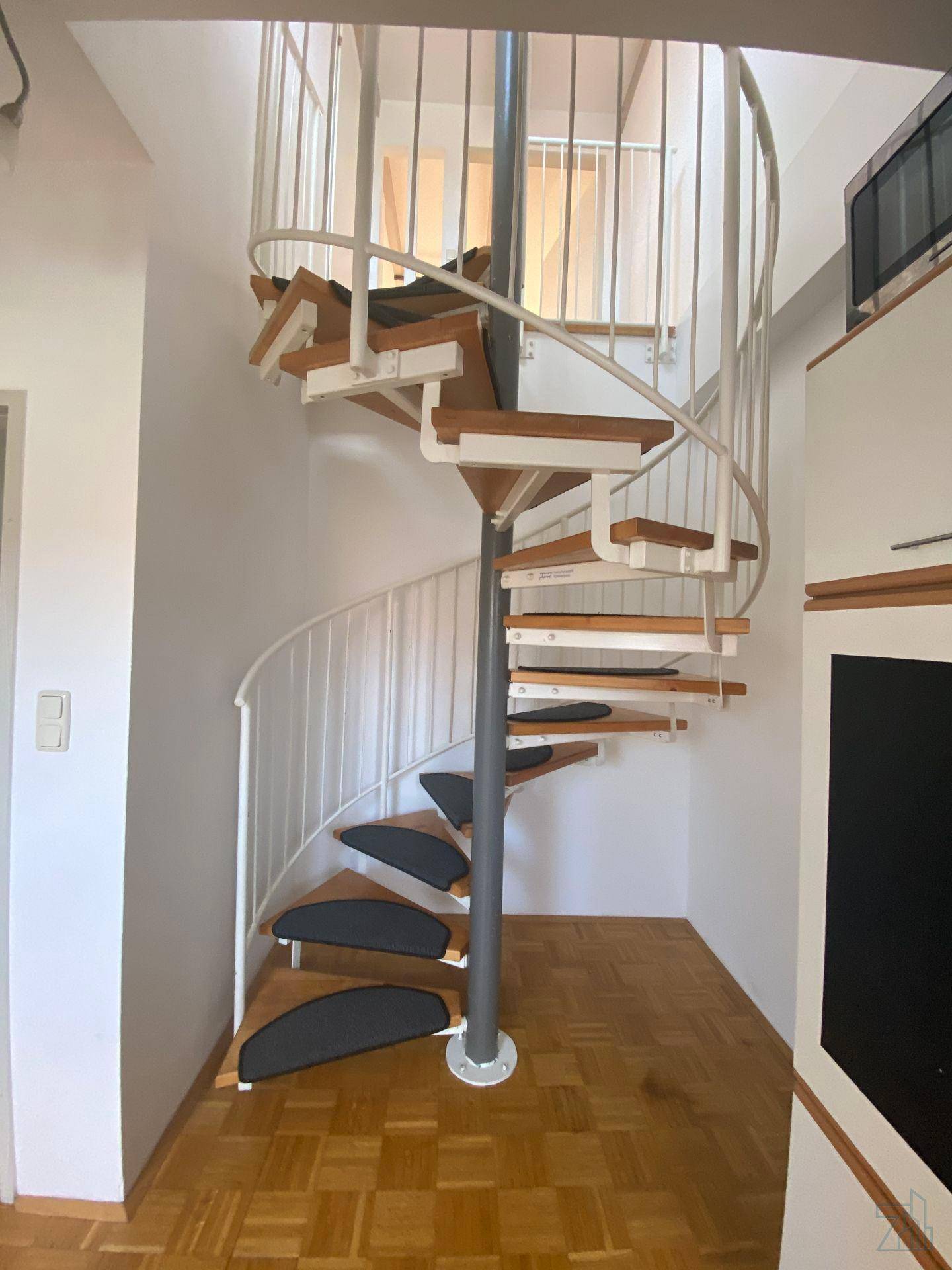 Elegante Wendeltreppe mit Holzstufen und Metallgeländer, die die Ebenen stilvoll verbindet.